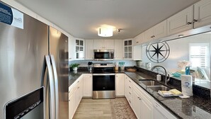 A modern kitchen with stainless steel appliances, white cabinetry, and a granite countertop. - Ocean Breeze West 301, 3BD/2BA, Community Pool + Private Beach (Perdido Key)