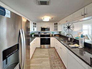 A modern kitchen with stainless steel appliances, white cabinetry, and a granite countertop.
