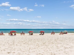 A beach with rows of sun loungers and umbrellas, a clear sky, and the ocean in the background.
