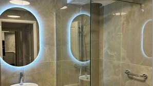 A modern bathroom with a glass-enclosed shower, a wooden vanity with a sink, and circular mirrors.