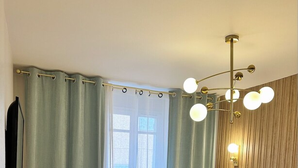 A hotel room with a bed, curtains, a wall-mounted light fixture, and a window.