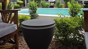 Et poolområde med et stråtækt tag, en pool og en bygning med et tegltag i baggrunden.