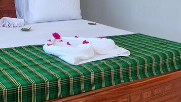 A neatly made bed with a green and white checkered bedspread, white pillows, and a white towel with a hat on it. There is a straw hat with the word "Hakuna" on it next to the bed.