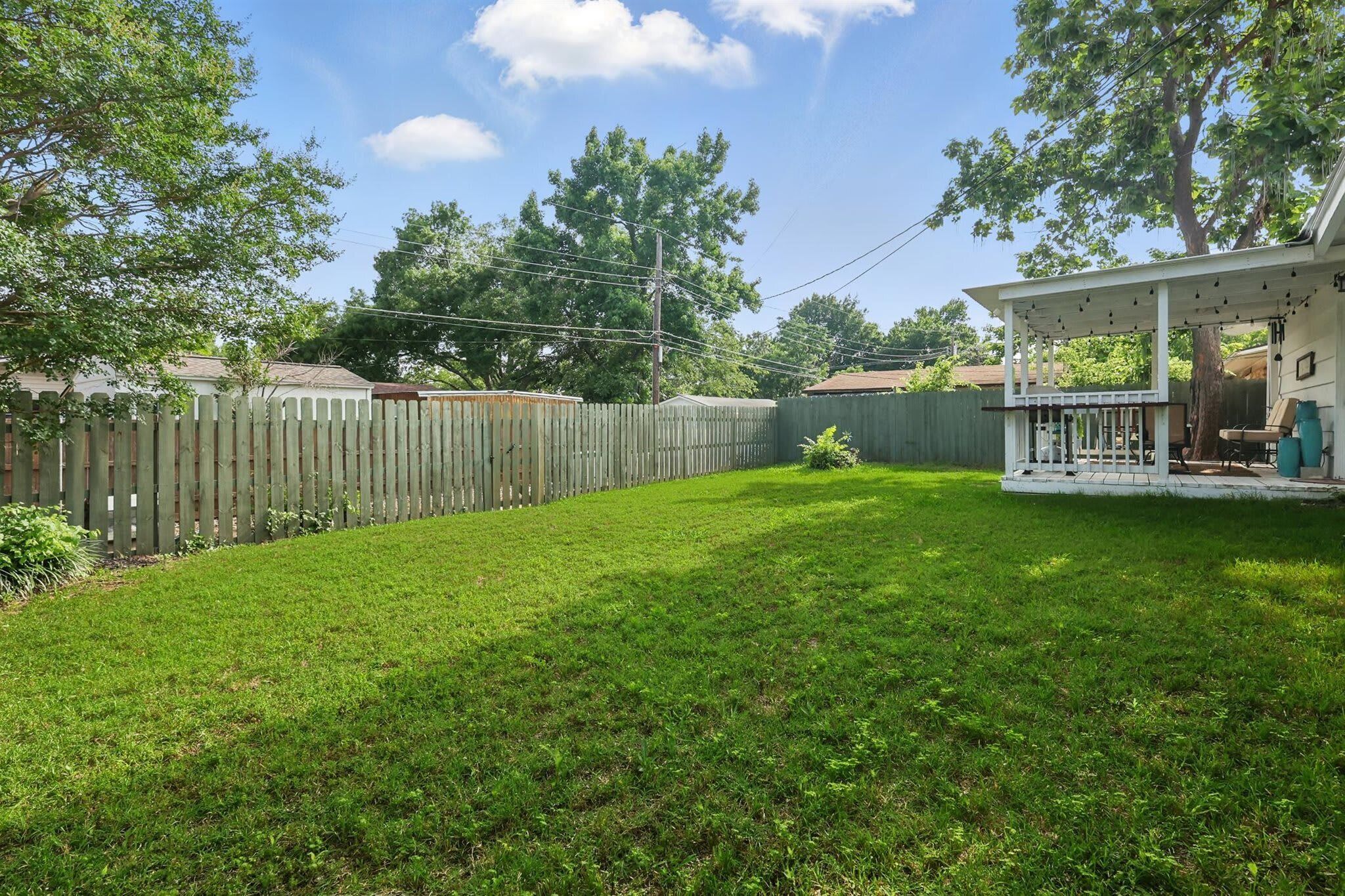 A backyard with a wooden fence, a lawn, and a house with a porch.