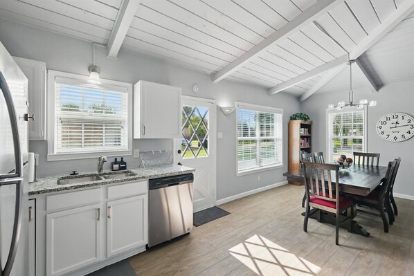 A kitchen with white cabinets, a dishwasher, and a dining area with a wooden table and chairs.