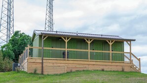 Il s’agit d’un petit bâtiment d’un seul étage, à l’extérieur vert et doté d’un porche en bois. Il est surmonté d’un toit en métal et est situé sur une colline herbeuse, avec des arbres en arrière-plan.