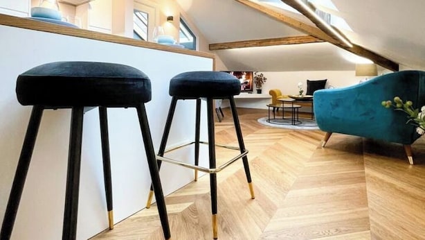 Ein modernes Loft mit hohen Decken, Holzbalken, einem blauen Sofa und zwei schwarzen Barhocker.