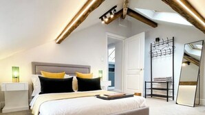 Ein modernes Schlafzimmer mit einem großen Bett, einem Nachttisch, einem Sessel, einem Spiegel und einem Oberlicht.