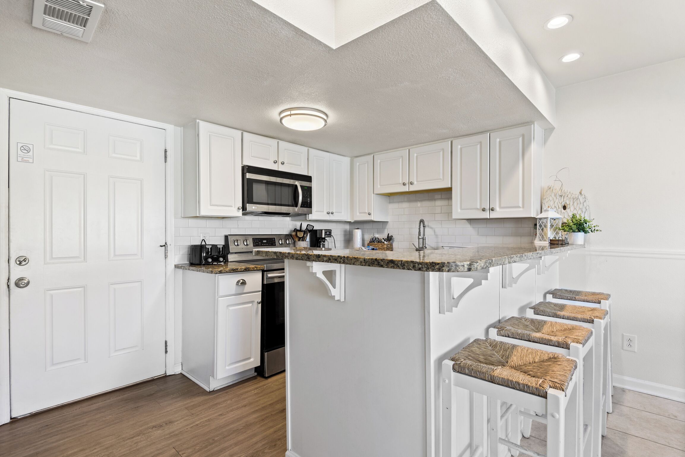 A kitchen with white cabinets, a microwave, a sink, and a bar stool area.