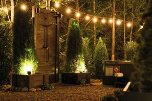 An outdoor area with a wooden structure, possibly a sauna or hot tub, surrounded by trees and illuminated by string lights. - Villa Sol-Mirror Cabin-Private-Hot Tub-FirePit-Luxury (Sevierville)