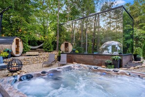 Un jacuzzi rodeado por una terraza de madera, con una hamaca y estructuras de madera rústica en un área boscosa.