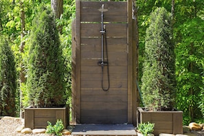 A wooden outdoor shower enclosure surrounded by dense greenery. - Villa Sol-Mirror Cabin-Private-Hot Tub-FirePit-Luxury (Sevierville)