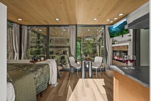 A modern room with a bed, a dining table with chairs, a TV, and a fireplace.