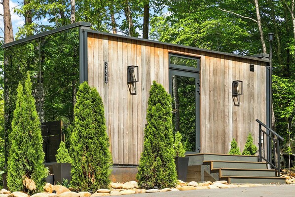 Una cabaña de madera con una puerta metálica, escalones y dos luces de estilo farol.
