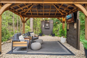 Un espacio de estar al aire libre cubierto con una pérgola de madera, un dardo y una chimenea.