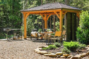 Un mirador de madera con mobiliario exterior y un sendero de grava y rocas.