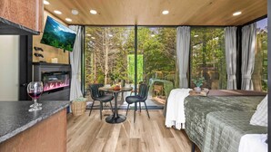 Una habitación acogedora con una cama, televisión, chimenea, zona de comedor y ventanas amplias.