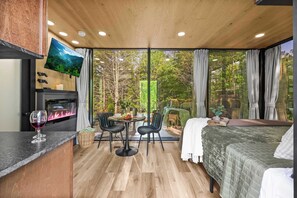 Una habitación acogedora con una cama, televisión, chimenea, zona de comedor y ventanas amplias.