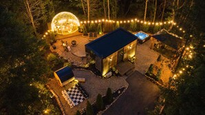 Una cabaña aislada rodeada de árboles, con una gran estructura esférica y un jacuzzi.