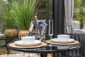 Una mesa dispuesta con platos blancos, un vaso y un recipiente decorativo con una botella.