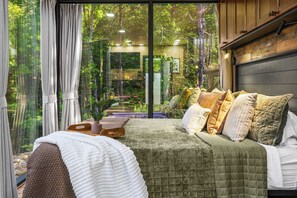 Un dormitorio con una cama grande, vista a espacios verdes por la ventana y un cabecero de madera.