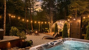 Un jacuzzi rodeado por una terraza, luces colgantes y un brasero.