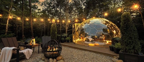 Un espacio al aire libre con zona de estar, una chimenea y una estructura abovedada de cristal.