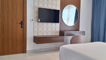 A modern bedroom with a large bed, a TV mounted on a wooden panel wall, a round mirror, and a built-in vanity with a sink.