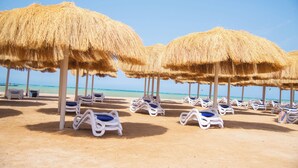 A beach with rows of sun loungers under thatched umbrellas, a clear blue sky, and the ocean in the background. - Rewaya Majestic Resort (Hurghada)
