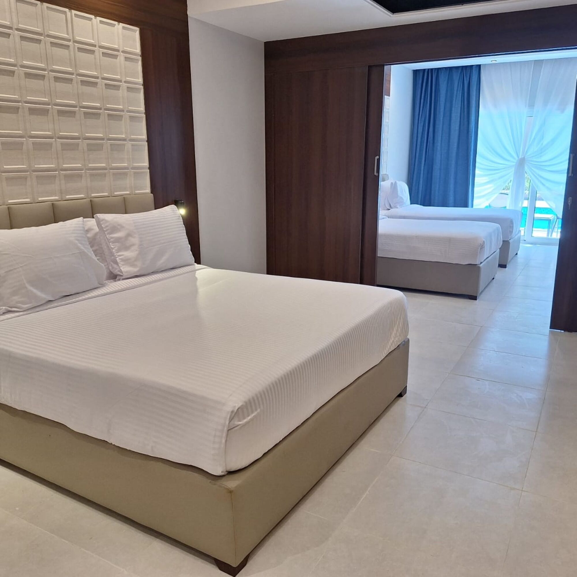 A modern hotel room with a large bed, a smaller bed, and a view of a pool area.