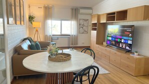 Ein modernes Wohnzimmer mit einem runden Esstisch, einer Couch, einem Fernseher und einer kleinen Pflanze.