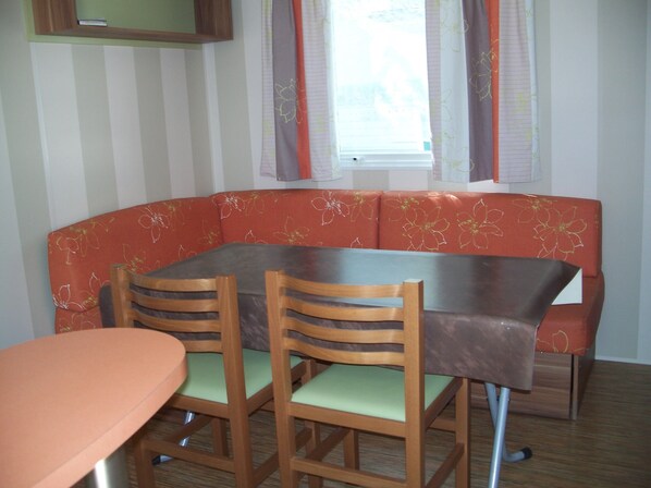Ein Essbereich mit Tisch und zwei Stühlen, eine Bank mit floralem Bezug und ein Fenster mit Vorhängen.