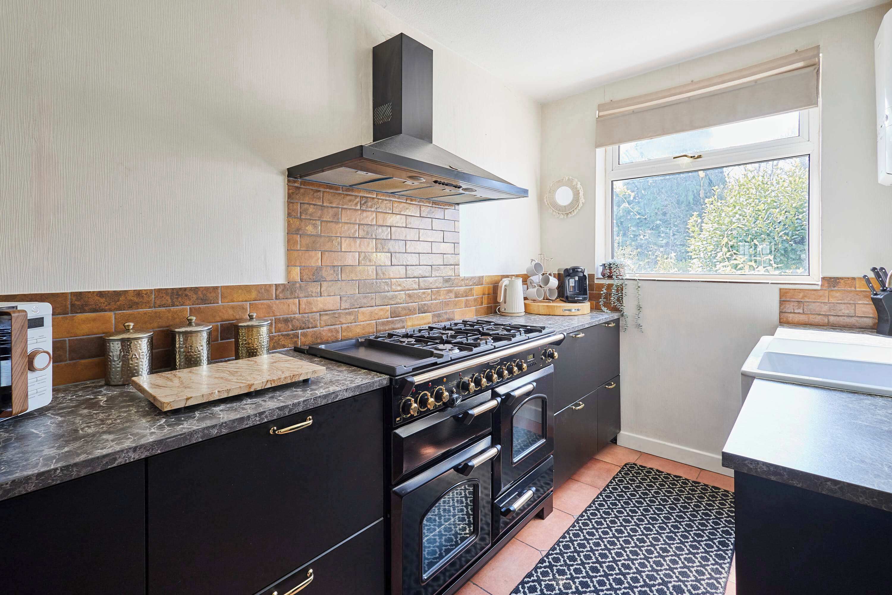 A kitchen with a gas stove, oven, and a window with a view of trees.