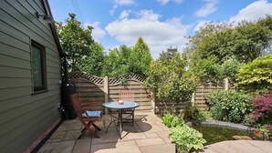 A patio with a table and chairs, surrounded by a wooden fence and lush greenery. - Host & Stay | Garden Studio (Hartlebury)