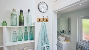 A bathroom with a white sink, a mirror, and shelves with vintage glass bottles. - Host & Stay | Garden Studio (Hartlebury)