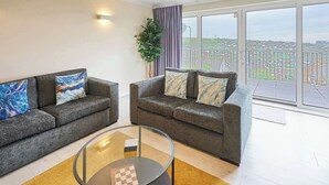 A living room with two grey sofas, a glass coffee table, and a large window offering a city view.