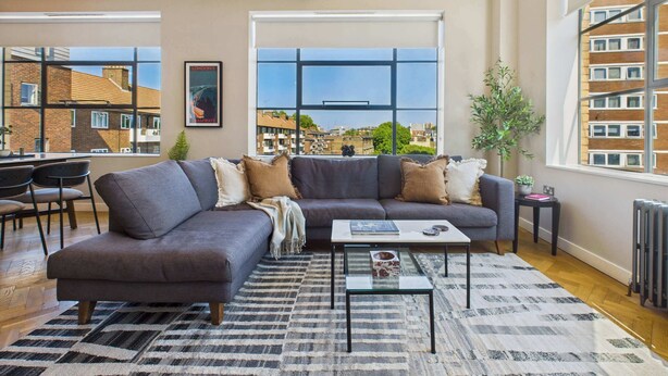 A modern living room with a sofa, coffee table, and large windows offering a city view. - Spacious and Bright Apartment by Tech City (Greater London)