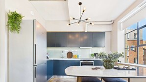 A modern kitchen with a central island, dark cabinetry, and a large window providing a view of the city. - Spacious and Bright Apartment by Tech City (Greater London)