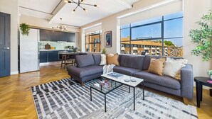A modern living room with a grey sofa, a coffee table, and a view of a cityscape through large windows. - Spacious and Bright Apartment by Tech City (Greater London)
