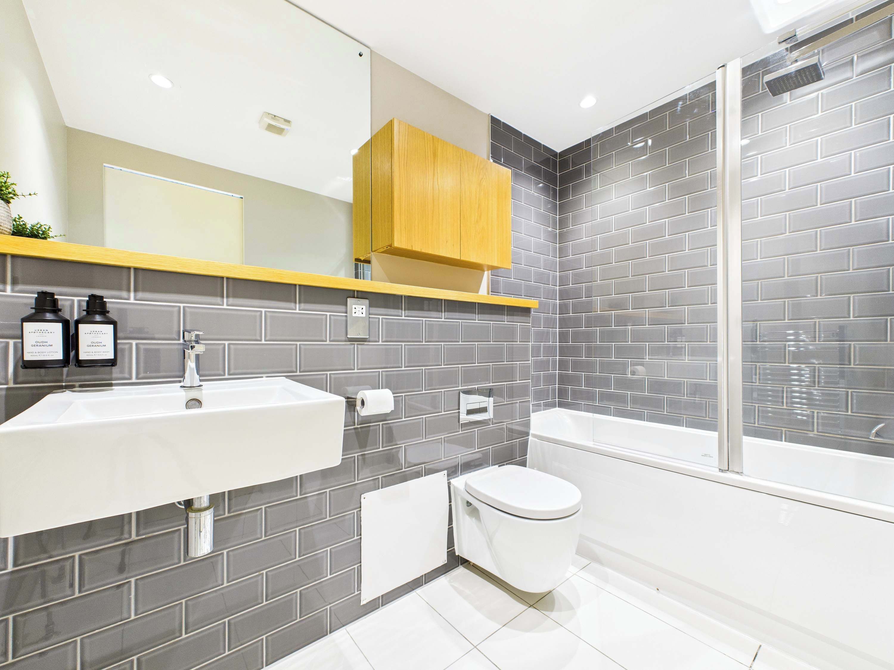 A modern bathroom with a white sink, a toilet, and a bathtub. There is a wooden cabinet above the sink and a shower area with a glass door.