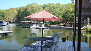 A deck with a table and chairs, overlooking a calm body of water with boats and a dock.