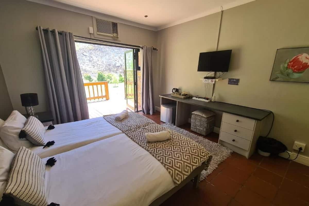 Une chambre d’hôtel avec deux lits, un bureau, une télévision et un balcon avec des rideaux.