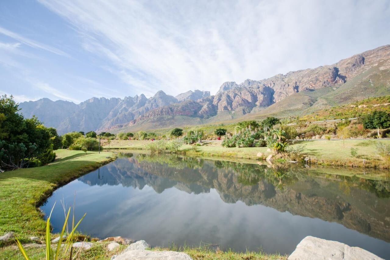 A tranquil lake with a clear reflection, surrounded by lush greenery and mountains in the background.