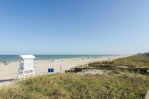 A beach with a lifeguard tower, beach umbrellas, and a grassy area in the foreground. - Cozy 1 Bedroom Condo in Carolina Beach - C329 (Carolina Beach)