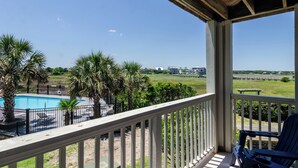 A balcony with a pool, palm trees, and a view of a bridge and buildings.