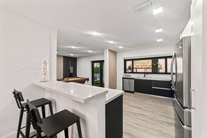 Une cuisine moderne dotée d’un îlot central, de tabourets de bar et d’un four encastré.
