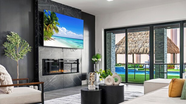 Una sala de estar moderna con televisor grande, chimenea y vista a una piscina y playa.