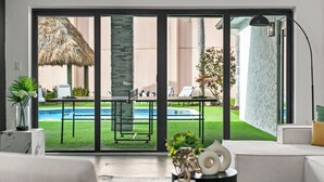 Una sala de estar moderna con un amplio ventanal corredera que da a una zona de piscina.