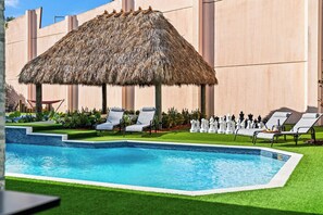 A swimming pool with a thatched umbrella, lounge chairs, and chess pieces.