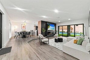 Un salon moderne avec un canapé, un coin repas avec des chaises, une cheminée et une vue sur une piscine.
